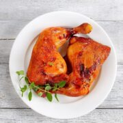 two roasted chicken leg quarters served on a white plate with herb garnish