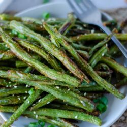Crispy air fried green beans garnished and served on a white plate on a light woven dinner mat. For on the plate.