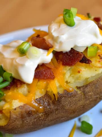 Air fryer baked potato close up topped with shredded cheese, chopped bacon, sour cream and sliced green onions.