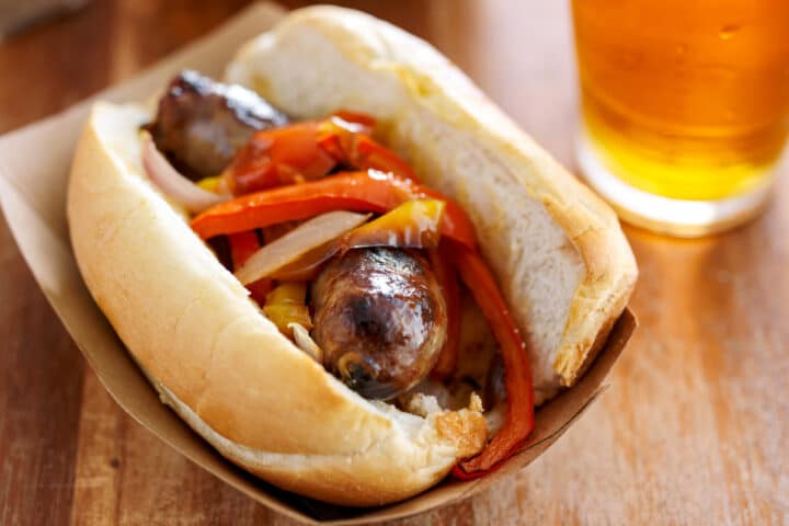 johnsonville brat in a bun with pepperss served with a beer