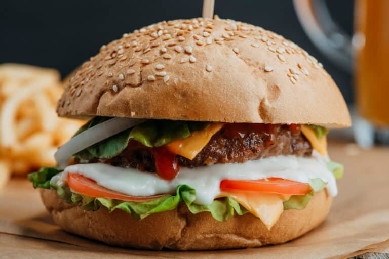 Closeup of air fryer burgers with lettuce, tomato, sauce, onion and cheese in a sesame bun.