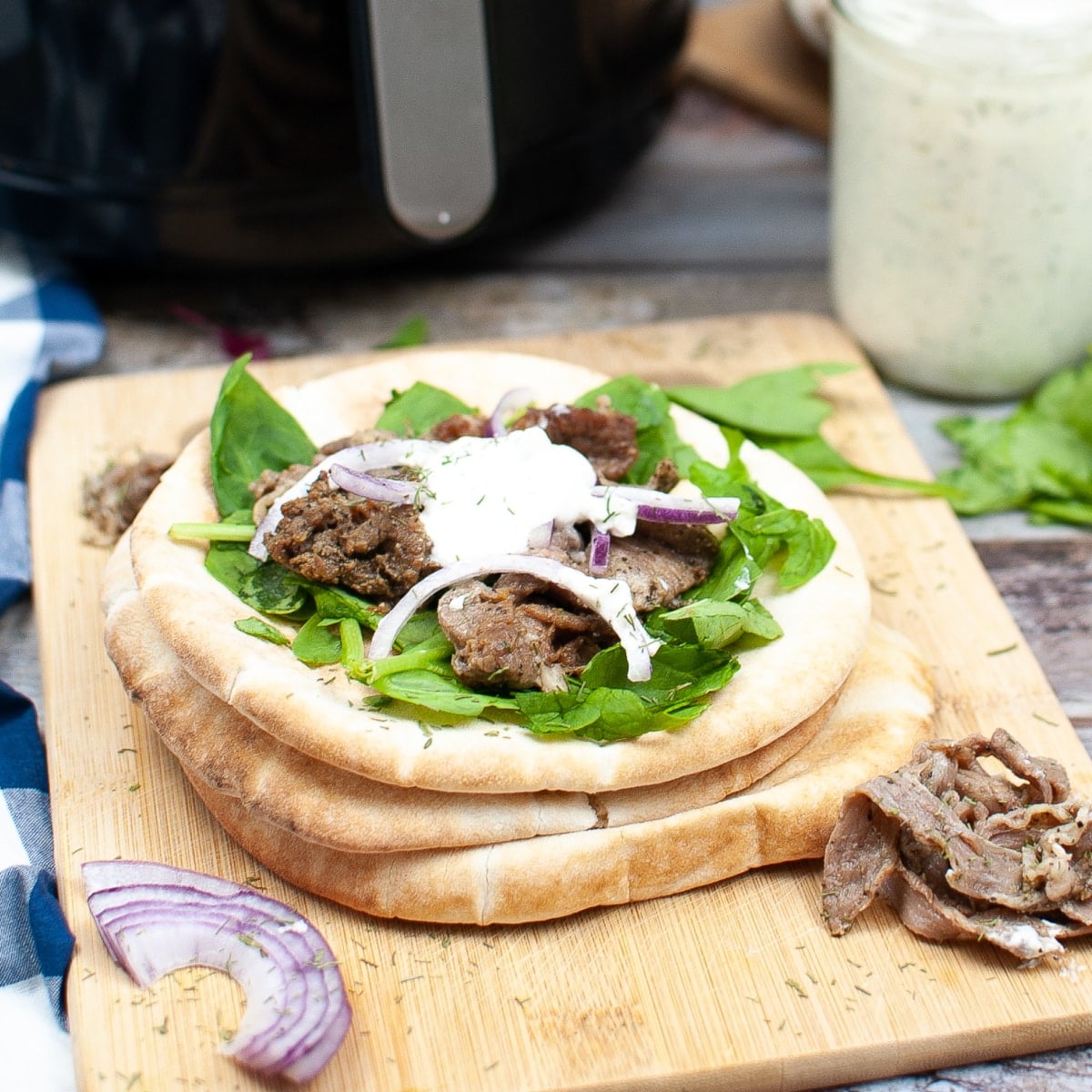 angled view of an gyro sandwich on a wood carving board. the gyro is topped with lettuce, seasoned shaved beef, onions and tzatziki sauce