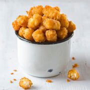 Air fryer tater tots in a little white metal bucket with a couple on the table.