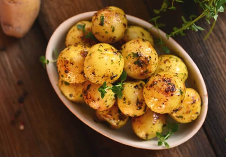 Baby Roast Potatoes in a red serving bowl. Potatoes are picture top down with herbs and spices.