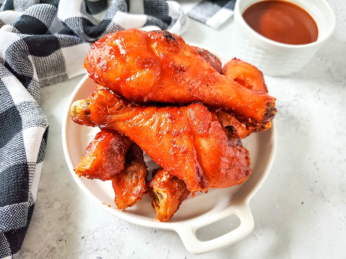 Baked bbq chicken legs on a white platter with a bowl of bbq sauce.