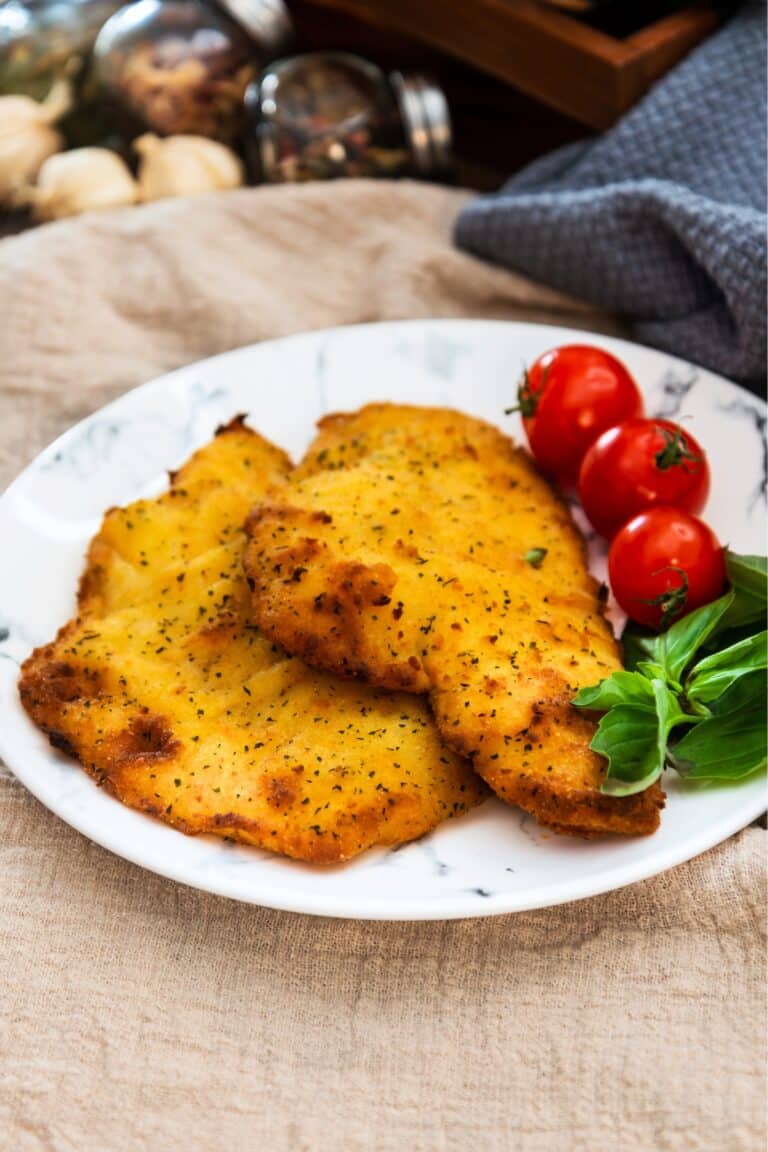 2 pieces of baked flounder on a plate with fresh tomatoes.