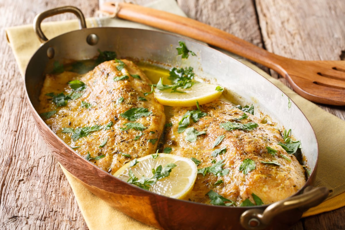 baked tilapia filets in a roasting pan with lemon and parsley