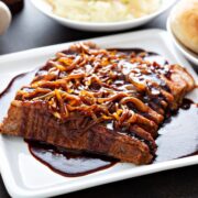beef brisket served on a white plate with caramelized onions on arranged over the top