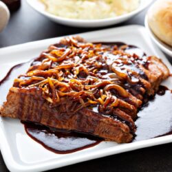 beef brisket served on a white plate with caramelized onions on arranged over the top