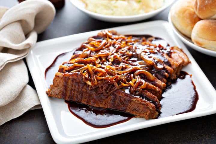 beef brisket served on a white plate with caramelized onions on arranged over the top