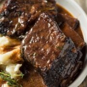 a bowl of beef short ribs with sauce and mashed potatoes