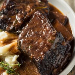 a bowl of beef short ribs with sauce and mashed potatoes
