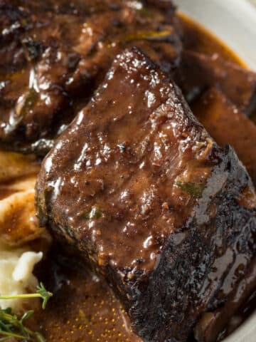 a bowl of beef short ribs with sauce and mashed potatoes