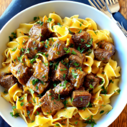overhead view of beef tips and gravy over wide egg noodles in a white bowl