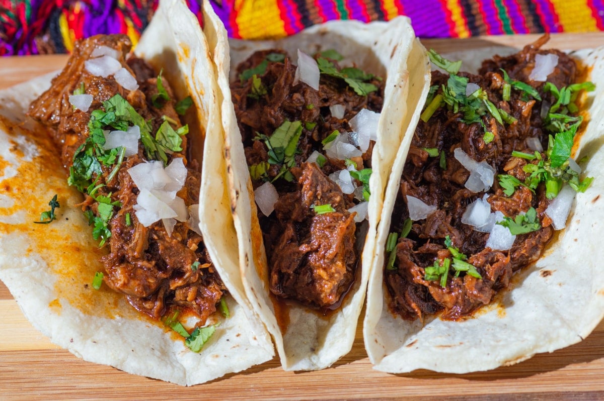 3 Birria tacos folded in half and served side by side on a wooden platter
