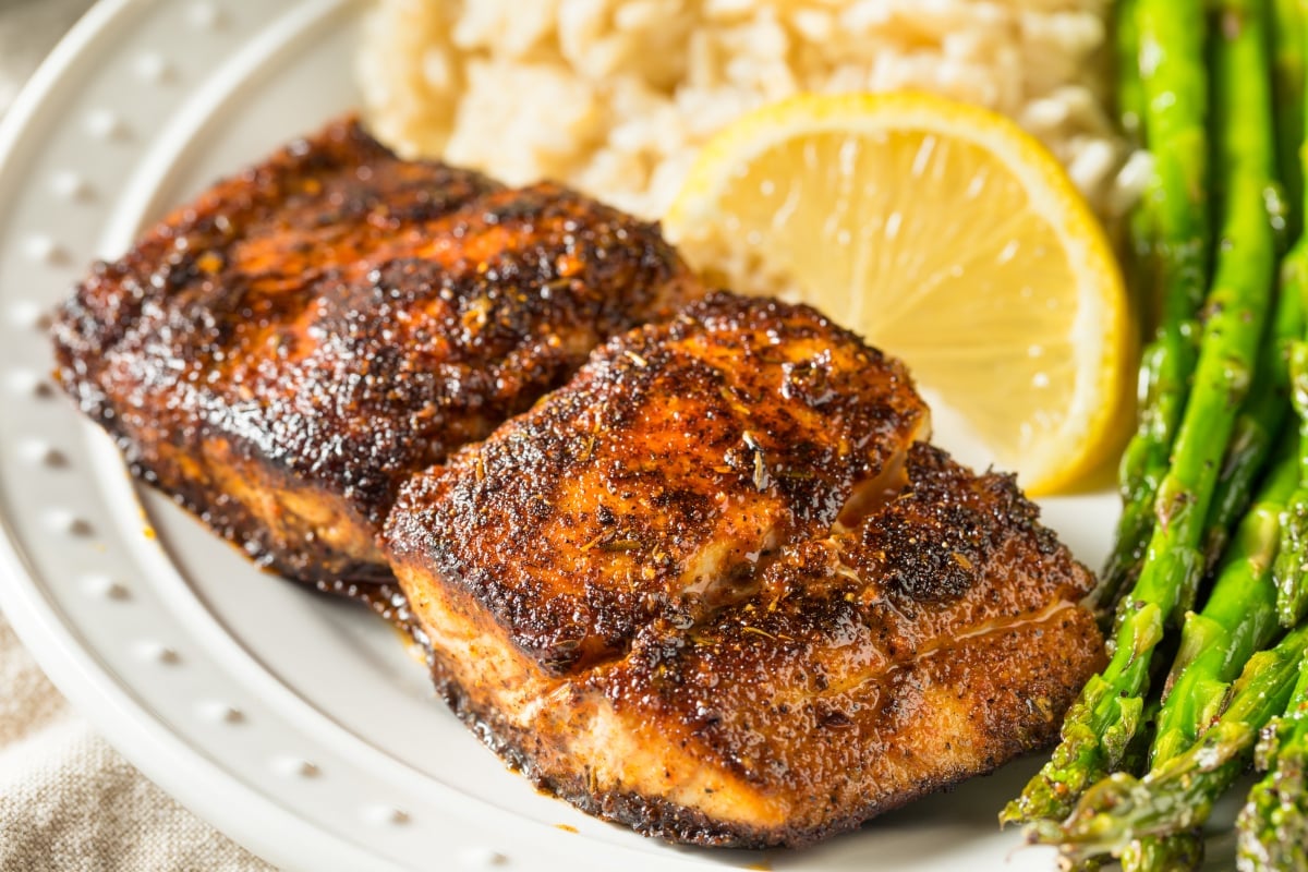 Blackened Mahi Mahi served on a white plate with rice, asparagus, and lemon slices.