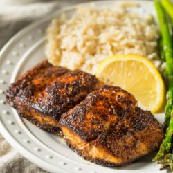 Blackened Mahi Mahi served on a white plate with rice, asparagus, and lemon slices.