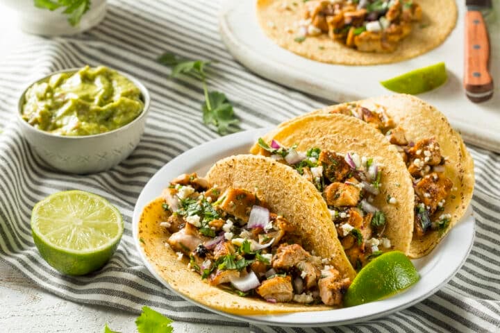 Chicken Tinga Tacos with sides of guacamole, limes and cilantro