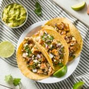 3 Chicken Tinga served on tacos. 3 tacos are on the plate with 1 chicken tinga laying flat and being assemble in the background