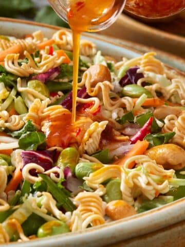 closeup of Chinese slaw recipe being drizzled with the ramen noodle dressing. hero shot of recipe.