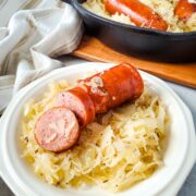 classic skillet kielbasa and sauerkraut recipe served on a white plate. partial view of recipe in the skillet in the background.