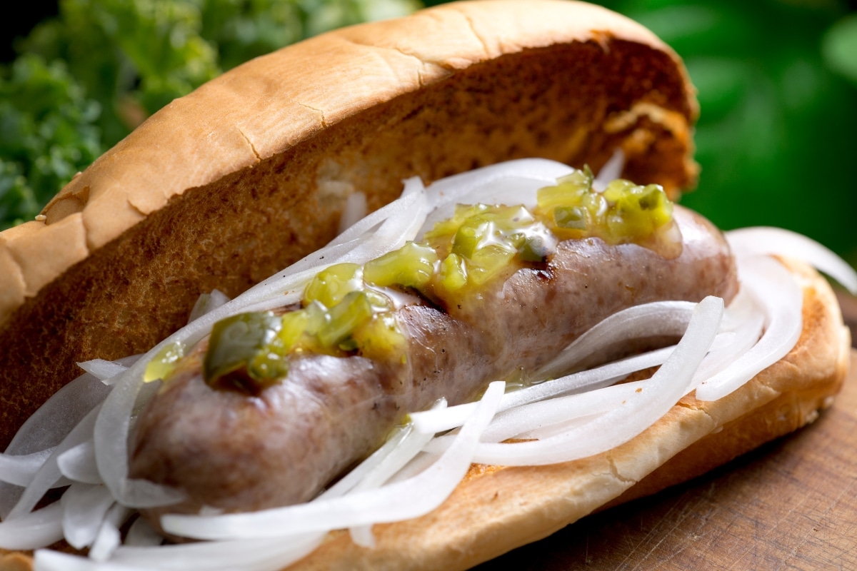 cooked bratwurst in a bun garnished with onions and pickle relish