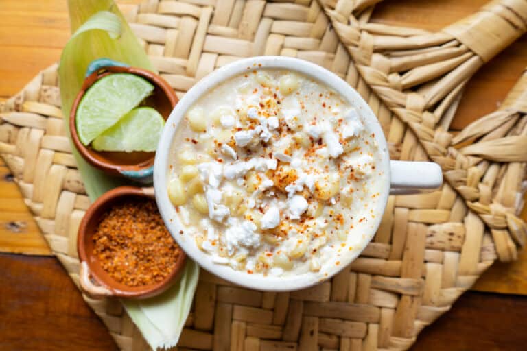 top down view of Mexican corn in a cup served with lime wedges and chili pepper on the side