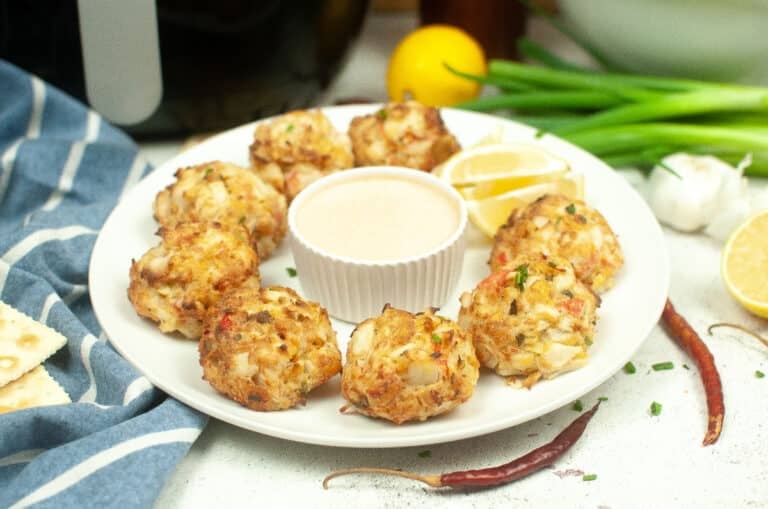 air fryer crab cakes arranged on a plate with sauce and lemon wedge