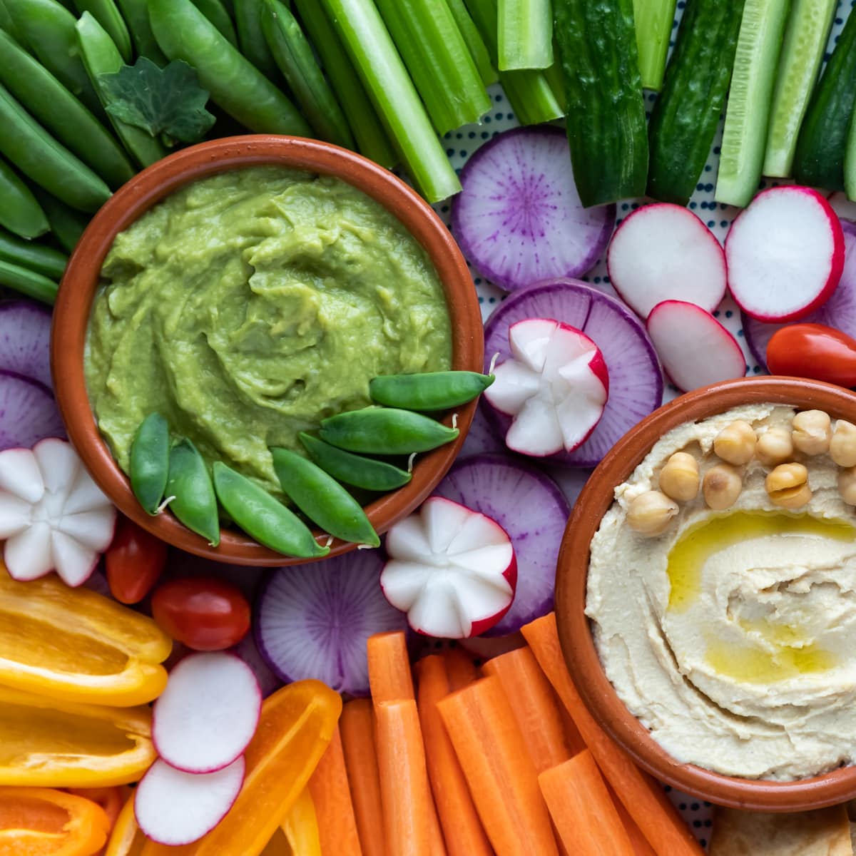 a veggies tray with 2 dips and an assortment of broccoli, carrots, celery, cherry tomatoes and cauliflower