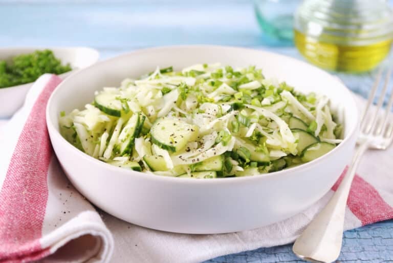 Cucumber, onion and vinegar salad garnished with a bit of dill. Salad is in a white bowl on a red and white striped napkin.