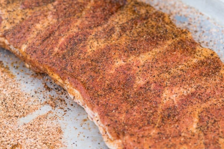 slab of raw beef back ribs on a sheet pan generously sprinkled with dry rub