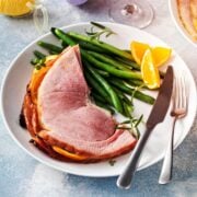 perfectly heated spiral ham slices on a plate with green beans and orange wedges served for Easter