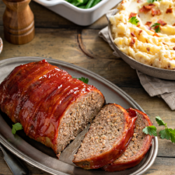 meatloaf sliced on a platter for servings with side dishes of mashed potatoes and green beans