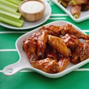 baked buffalo chicken wings served on a white platter on a football field themed tablecloth.