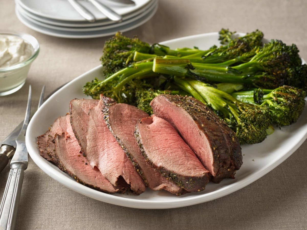 top round roast carve on a white serving platter with broccolini served alongside