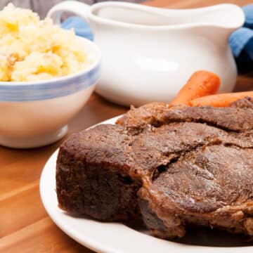 Closeup of oven baked chuck roast recipe with carrots, potatoes and gravy on the side