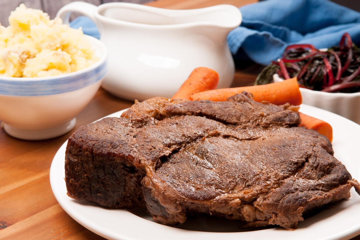 beef chuck roast on a white platter with sides and gravy