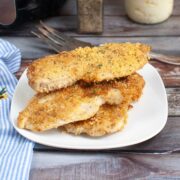 crispy pieces of parmesan crusted chicken sitting on a plate with a fork and blue striped napkin