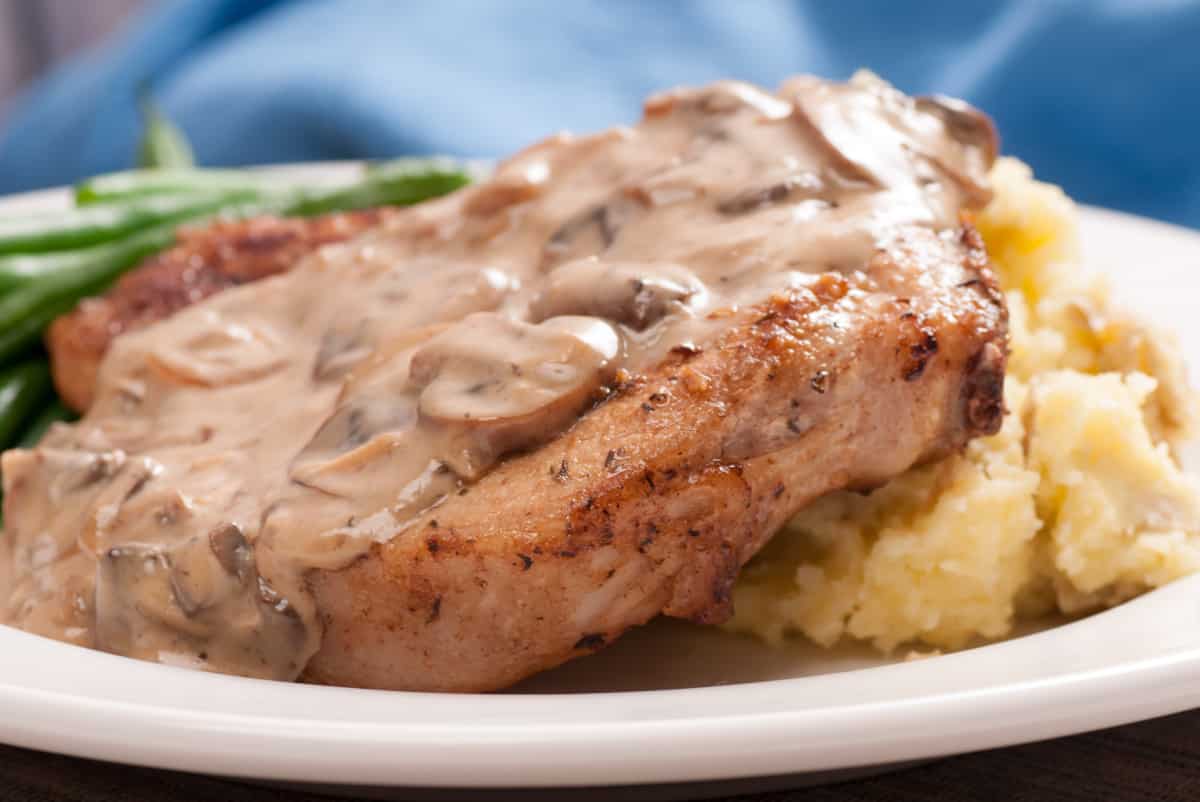 easy weeknight meals Pork Chops With Cream of Mushroom soup served on a white plate with mashed potatoes and g