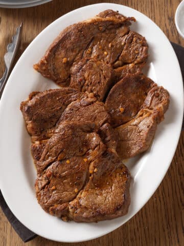 sauteed beef chuck steaks on a white serving platter