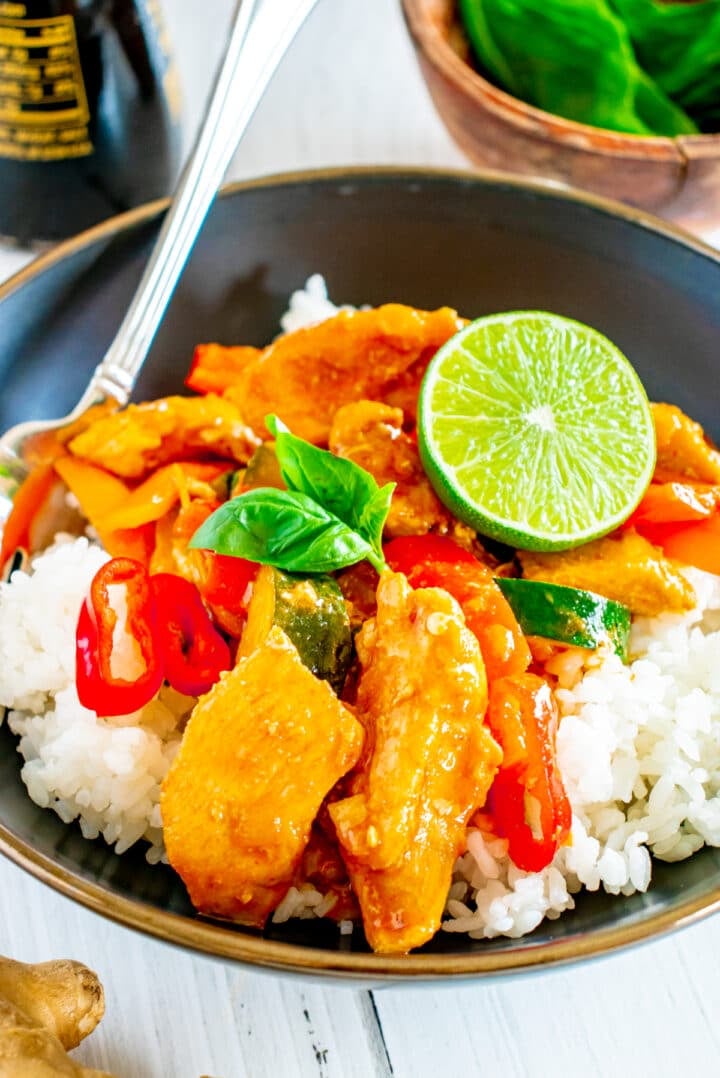 closeup of red curry chicken served on basmati rice and garnished with lime and Thai basil.