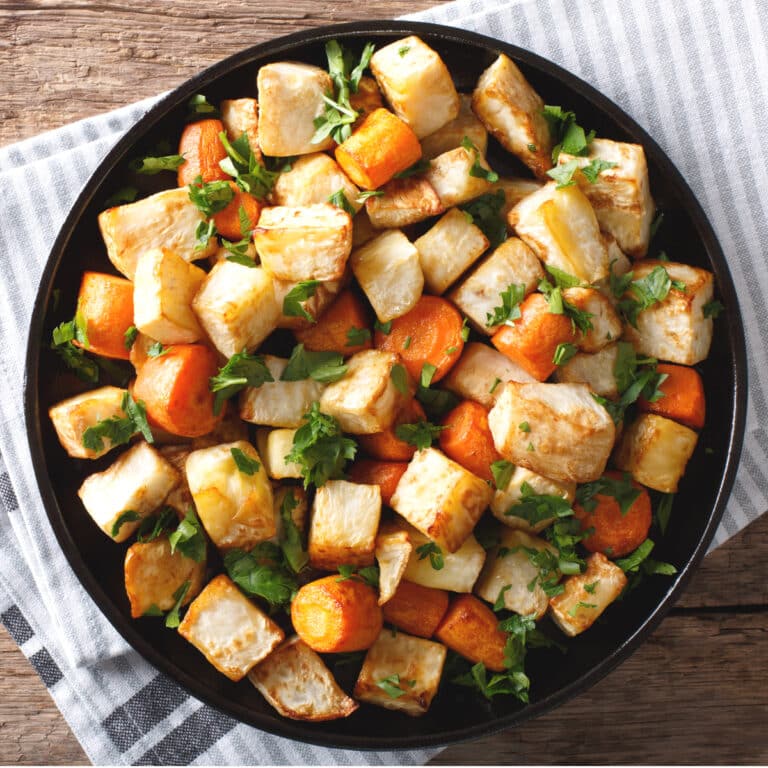 Roasted carrots and potatoes served in a bowl garnished with herbs. Top down view.