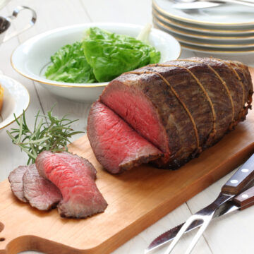 Carved rump roast on a wood carving board with a bowl of greens ready to be served.