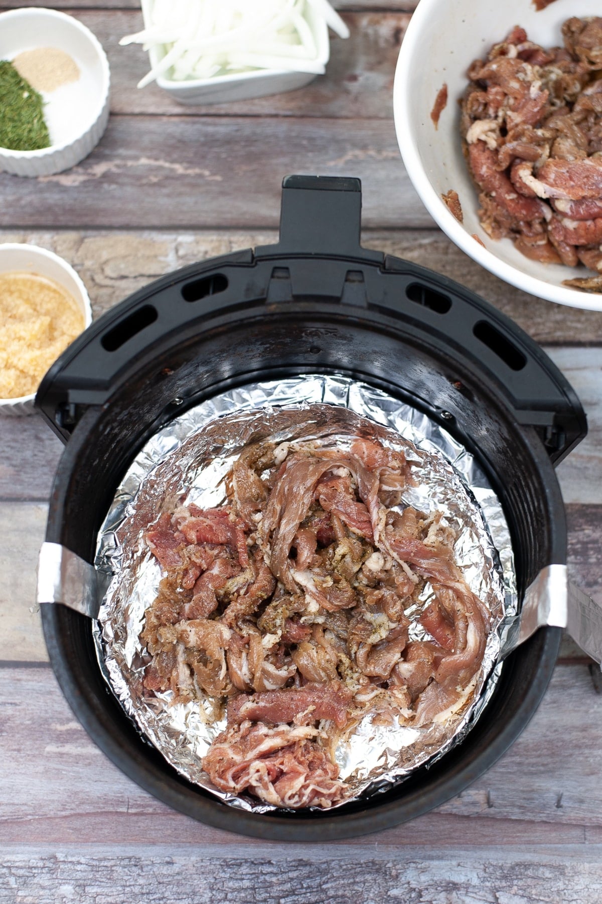 top down view of shaved marinated gyro meat in the air fryer. the air fryer is lined with foil to retain the meat's juices.