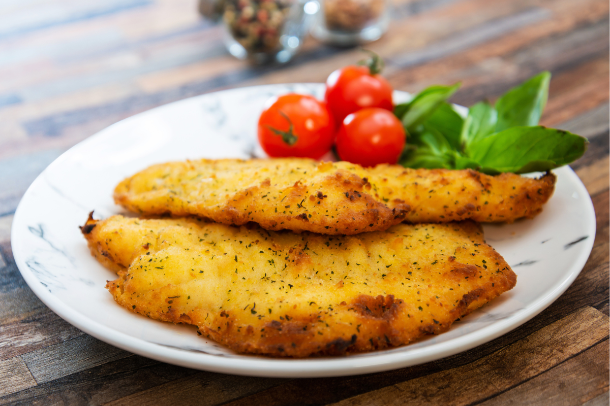 2 sheet pan flounder with breadcrumbs on a white plate with cherry tomatoes