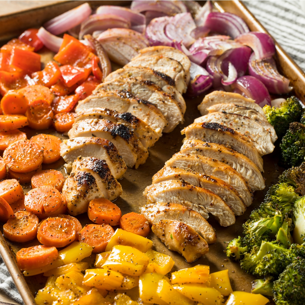sliced chicken and assorted vegetables on a sheet pan