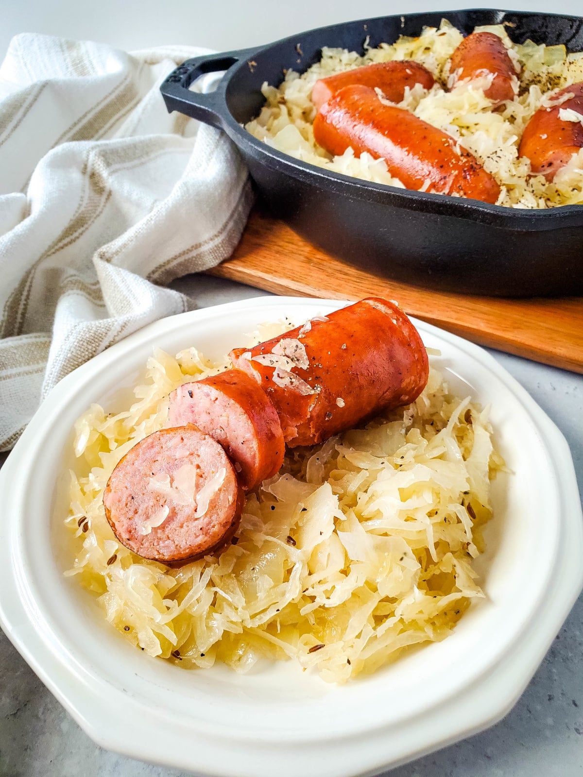 classic skillet kielbasa and sauerkraut recipe served on a white plate. partial view of recipe in the skillet in the background.