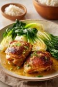 pan seared skillet miso butter chicken thighs with the bone-in and skin-on served with sauce, a side of rice and sauteed baby bok choy