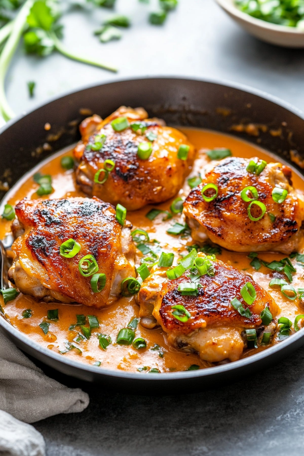 miso butter chicken thighs in sauce in a skillet, garnished with sliced green onions