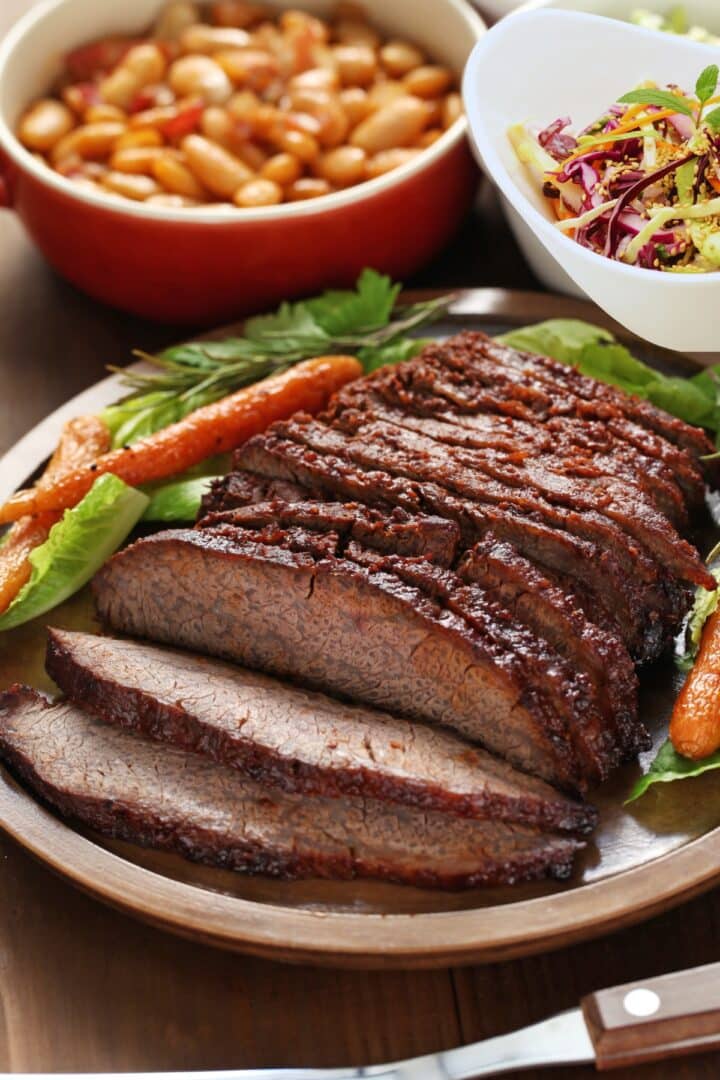 oven baked beef brisket sliced on a platter served with baked beans and slaw on the side